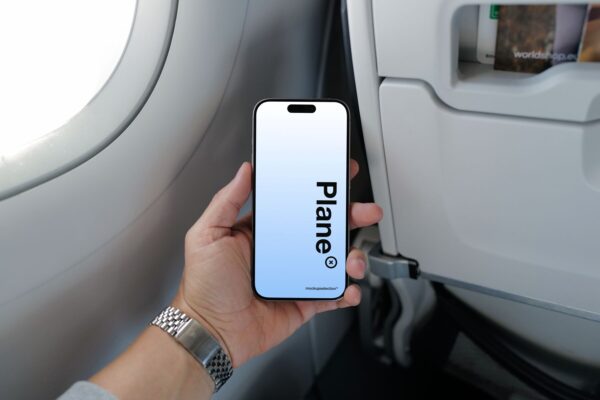 Hand holding an iPhone 15 Pro mockup in an airplane cabin next to a bright window.